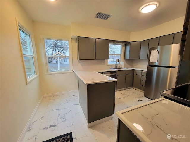 kitchen with kitchen peninsula, decorative backsplash, light stone counters, stainless steel appliances, and sink