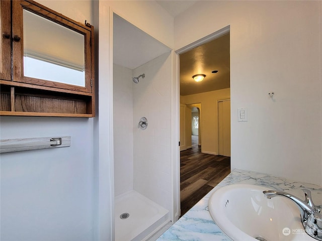 bathroom with hardwood / wood-style flooring, a tile shower, and sink