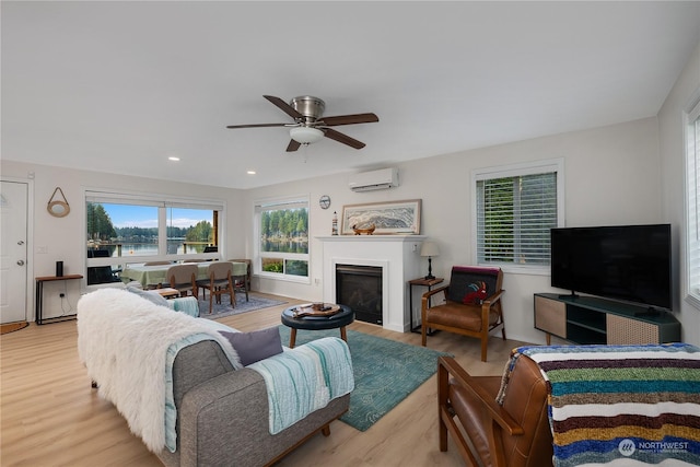 living room featuring ceiling fan, a wall mounted AC, and light hardwood / wood-style flooring