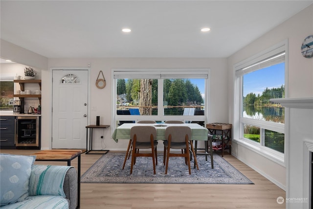 dining area featuring beverage cooler, light hardwood / wood-style floors, plenty of natural light, and a water view