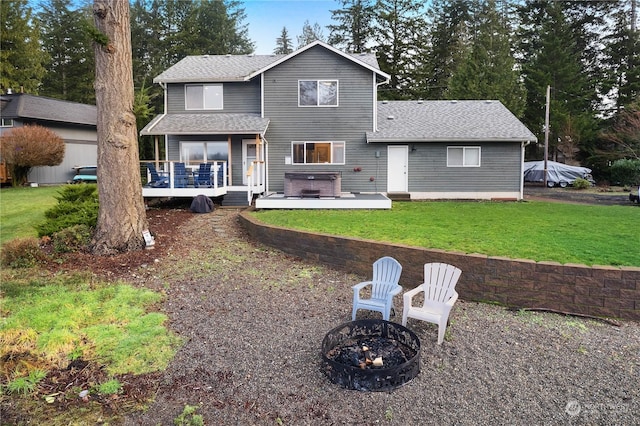 rear view of property featuring a yard, a fire pit, a hot tub, and a wooden deck