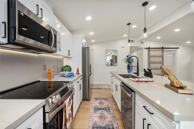 kitchen with white cabinets, vaulted ceiling, a barn door, light wood-type flooring, and appliances with stainless steel finishes