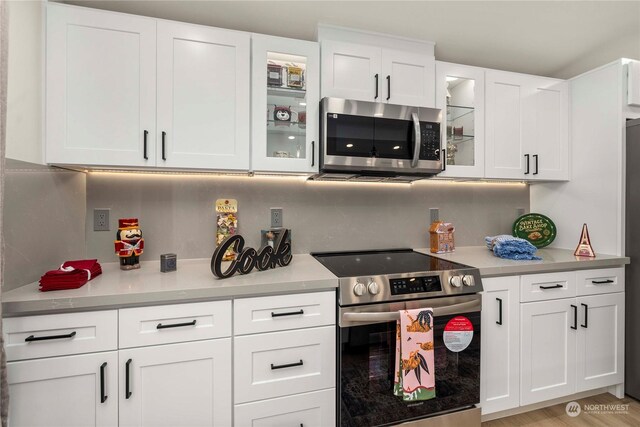 kitchen with white cabinets, decorative backsplash, light wood-type flooring, and stainless steel appliances