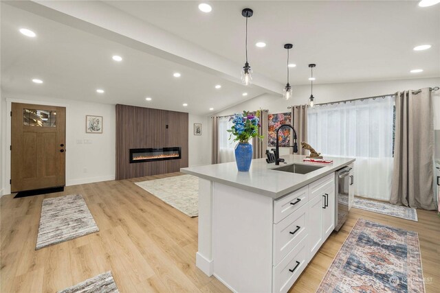 kitchen featuring a large fireplace, a kitchen island with sink, sink, vaulted ceiling with beams, and white cabinetry