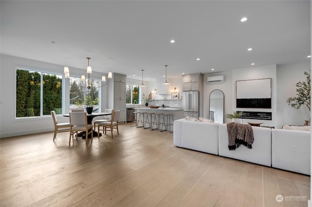 living room with a wall mounted AC, an inviting chandelier, and light wood-type flooring