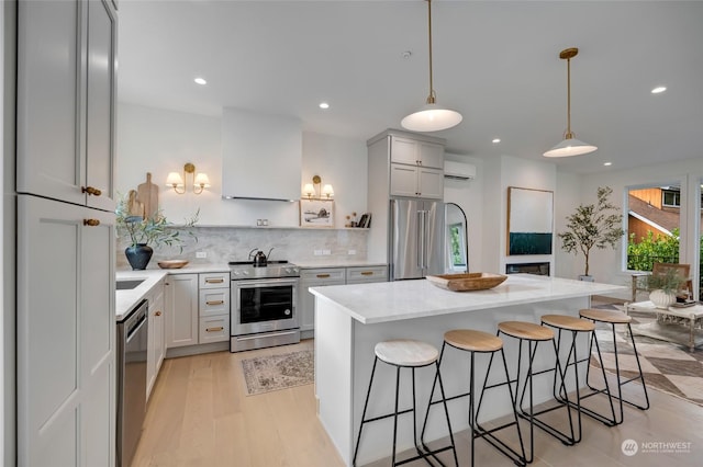 kitchen with pendant lighting, an AC wall unit, light wood-type flooring, appliances with stainless steel finishes, and a kitchen island