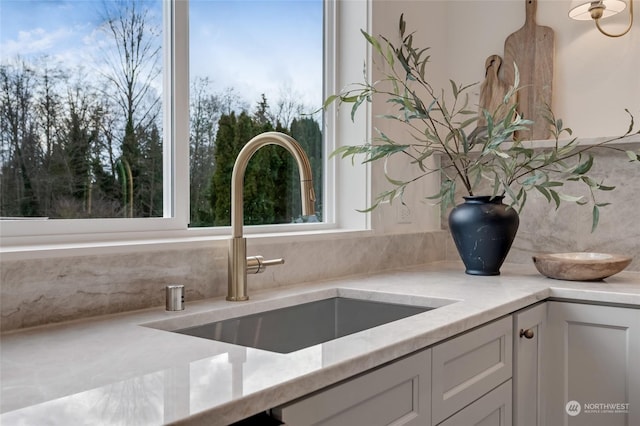 details with backsplash, light stone countertops, white cabinetry, and sink