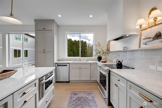 kitchen featuring a wealth of natural light, light stone countertops, stainless steel appliances, and exhaust hood