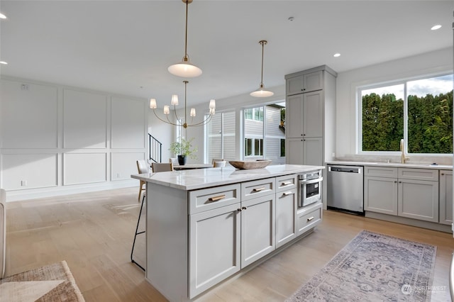 kitchen with a center island, hanging light fixtures, stainless steel appliances, light stone counters, and gray cabinets