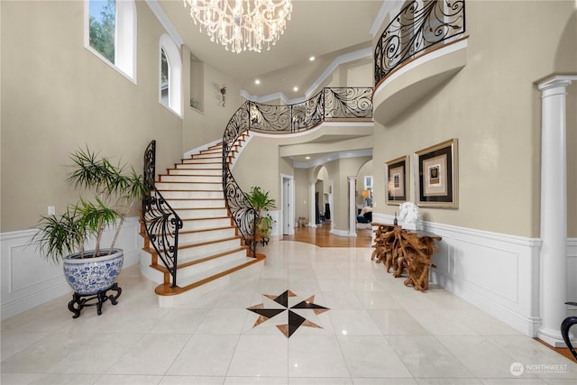 foyer entrance with a towering ceiling, a chandelier, and decorative columns