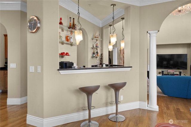 bar with decorative columns, ornamental molding, hardwood / wood-style flooring, and hanging light fixtures