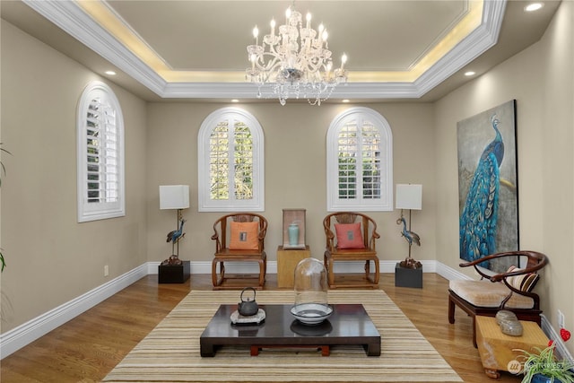 living area with light hardwood / wood-style floors, an inviting chandelier, crown molding, and a tray ceiling