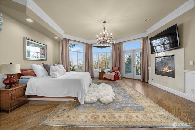 bedroom with access to outside, hardwood / wood-style flooring, an inviting chandelier, crown molding, and a tiled fireplace