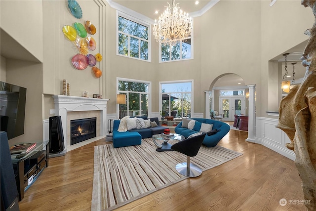 living room with a towering ceiling, an inviting chandelier, decorative columns, and hardwood / wood-style flooring