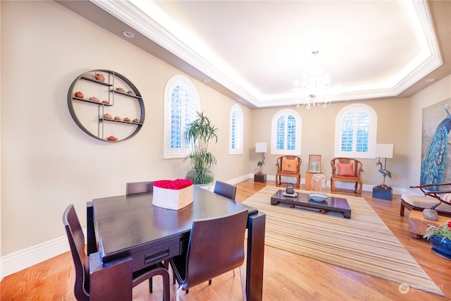 dining space with a healthy amount of sunlight, a notable chandelier, a raised ceiling, and wood-type flooring