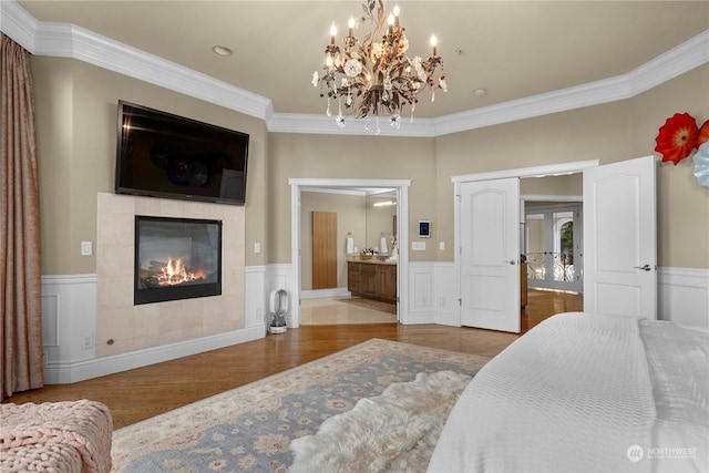 bedroom featuring a tile fireplace, crown molding, a notable chandelier, light hardwood / wood-style flooring, and ensuite bathroom