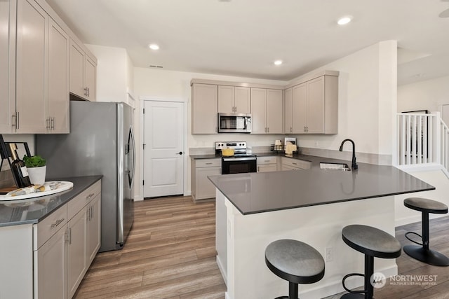 kitchen with a kitchen bar, sink, light wood-type flooring, kitchen peninsula, and stainless steel appliances