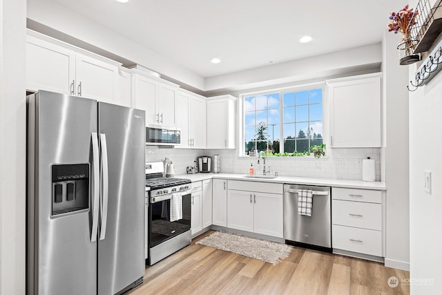 kitchen with backsplash, white cabinets, sink, light hardwood / wood-style flooring, and appliances with stainless steel finishes