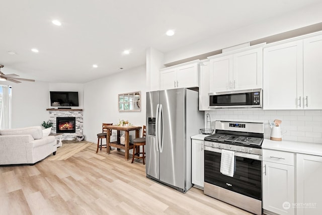 kitchen featuring appliances with stainless steel finishes, tasteful backsplash, a fireplace, ceiling fan, and white cabinets