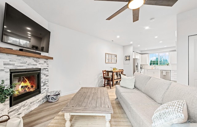 living room with a stone fireplace, ceiling fan, sink, and light hardwood / wood-style floors