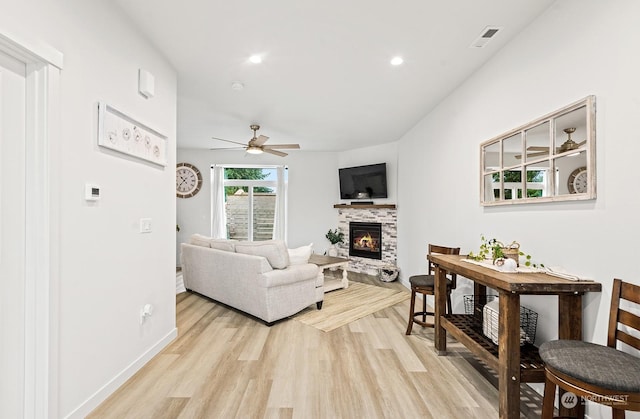 living room featuring light hardwood / wood-style floors, ceiling fan, and a tiled fireplace