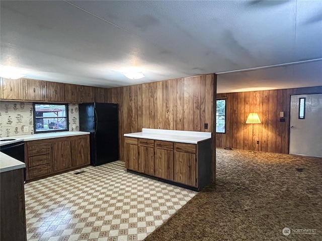 kitchen featuring a wealth of natural light, black refrigerator, dark brown cabinetry, and wooden walls