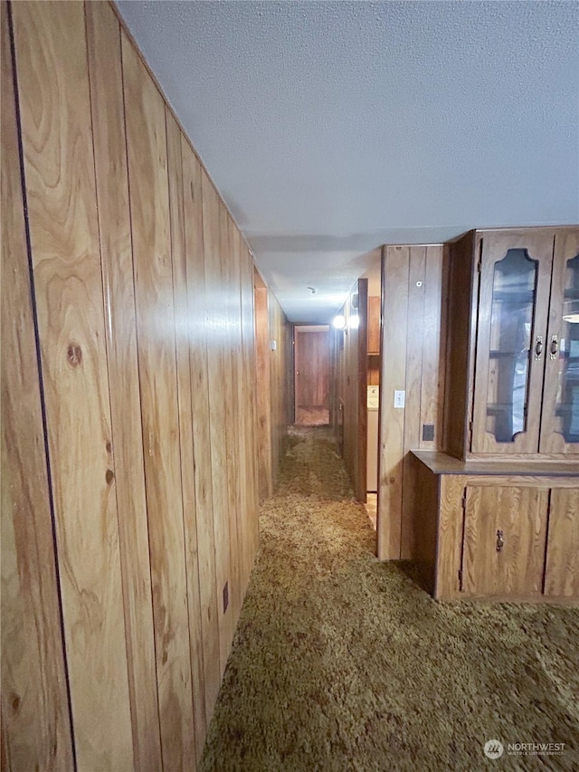 corridor featuring a textured ceiling, light carpet, and wood walls