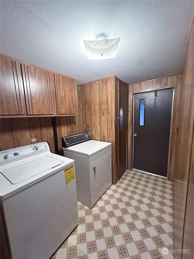 laundry area featuring separate washer and dryer, wood walls, cabinets, and a textured ceiling