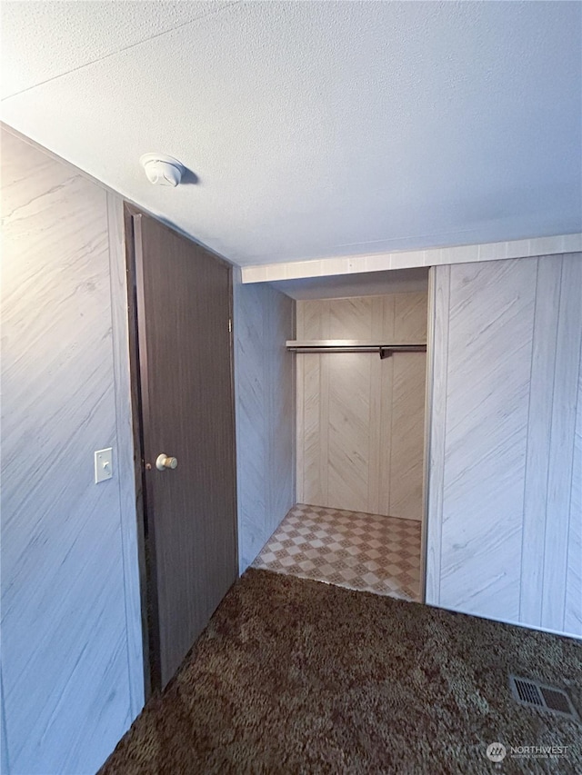 hallway featuring light colored carpet, a textured ceiling, and wooden walls