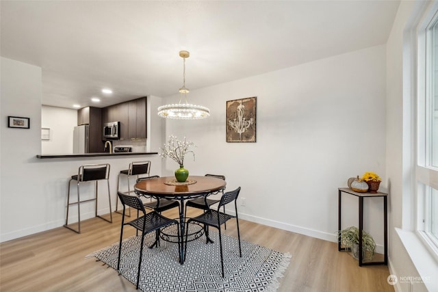 dining room with light wood-type flooring, sink, and an inviting chandelier