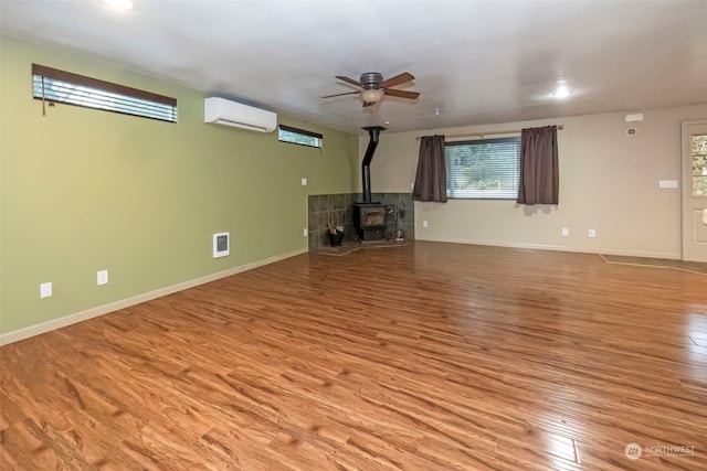 unfurnished living room featuring visible vents, an AC wall unit, a wood stove, light wood-type flooring, and baseboards