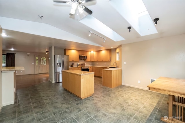 kitchen with vaulted ceiling with skylight, light brown cabinets, stainless steel appliances, a sink, and light countertops