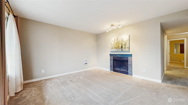 unfurnished living room featuring rail lighting, light colored carpet, and a fireplace