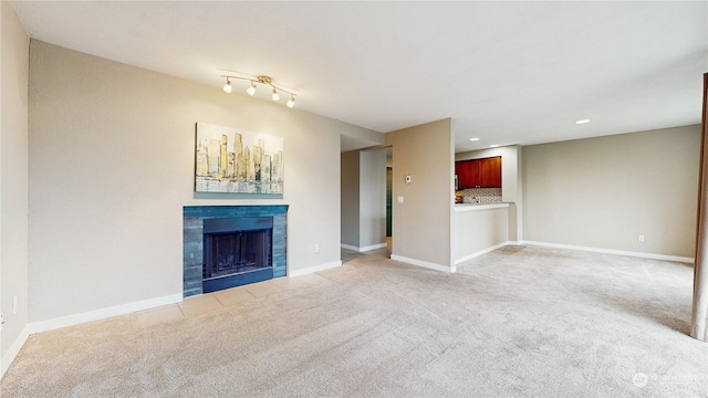 unfurnished living room featuring light colored carpet, rail lighting, and a tiled fireplace