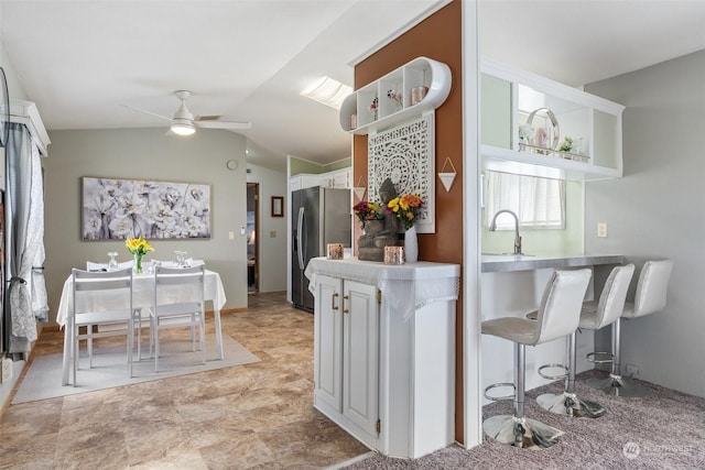 kitchen featuring sink, vaulted ceiling, ceiling fan, stainless steel fridge, and white cabinetry