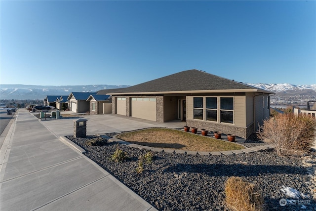 view of front facade with an attached garage, a mountain view, a shingled roof, concrete driveway, and stone siding