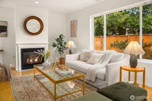 living room with a glass covered fireplace, recessed lighting, baseboards, and wood finished floors