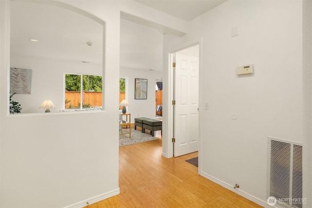 hallway featuring baseboards, visible vents, light wood finished floors, and arched walkways