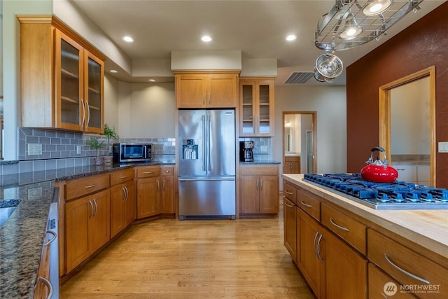 1078 Gardena Creek Rd, Touchet, WA 99360 - kitchen with stainless steel appliances, brown cabinets, light wood-type flooring, decorative backsplash, and glass insert cabinets