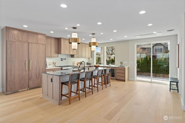 kitchen with dark stone counters, a kitchen island with sink, a breakfast bar, and light hardwood / wood-style flooring