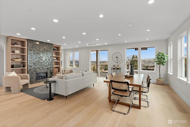 living room with a stone fireplace, built in shelves, and light hardwood / wood-style flooring