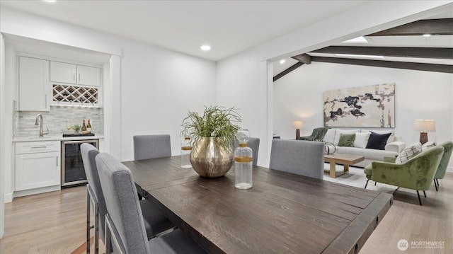 dining area featuring vaulted ceiling with beams, recessed lighting, beverage cooler, light wood finished floors, and indoor wet bar