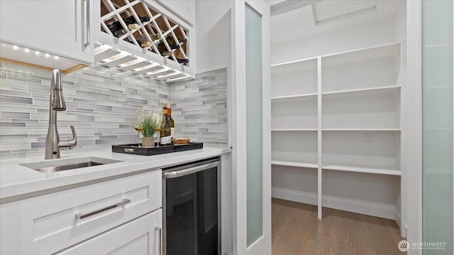 kitchen featuring tasteful backsplash, wine cooler, white cabinets, and a sink