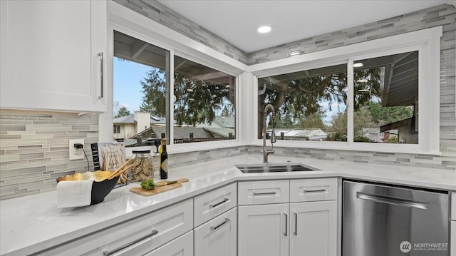 kitchen featuring backsplash, light countertops, stainless steel dishwasher, white cabinetry, and a sink