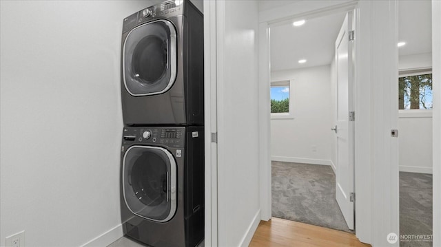 laundry area with stacked washer / drying machine, baseboards, and wood finished floors