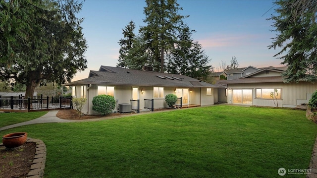 rear view of property featuring a lawn, fence, and central air condition unit