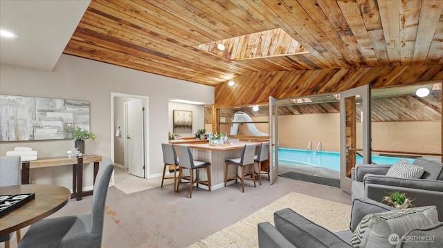 dining room with vaulted ceiling, wooden ceiling, baseboards, and concrete flooring