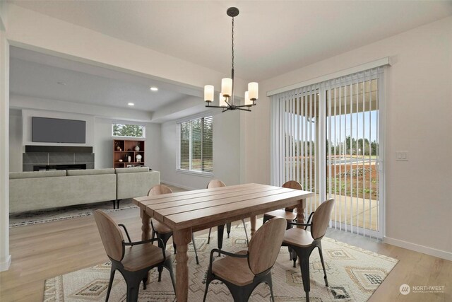 dining space with a tiled fireplace, light hardwood / wood-style floors, and an inviting chandelier