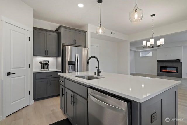 kitchen featuring appliances with stainless steel finishes, sink, a tile fireplace, pendant lighting, and an island with sink