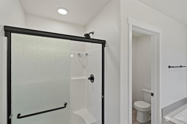 bathroom featuring a shower with door and toilet